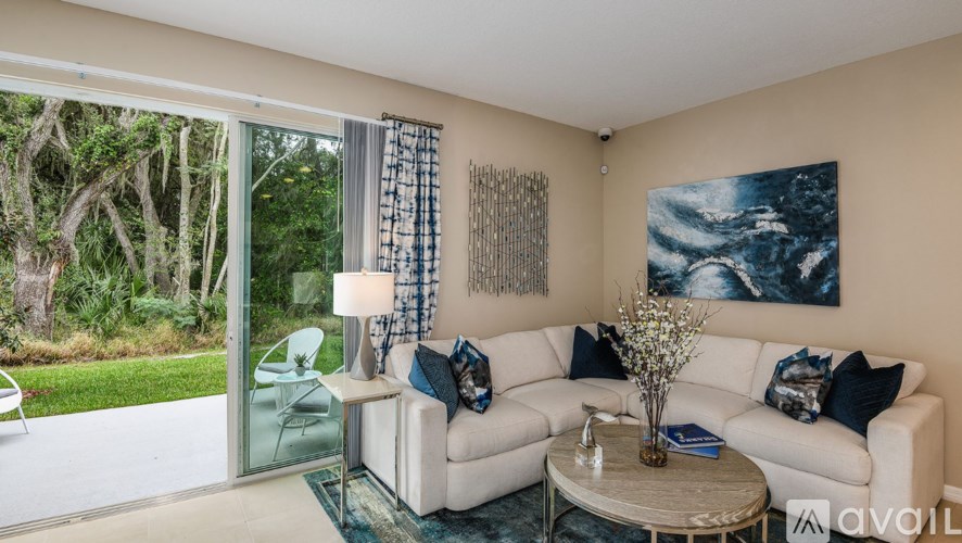 A living room with a white couch, a glass table, and a painting on the wall.