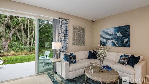 A living room with a white couch, a glass table, and a painting on the wall.