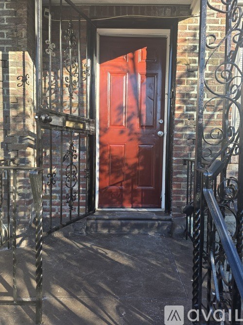 A red door is at the end of a black wrought iron staircase.