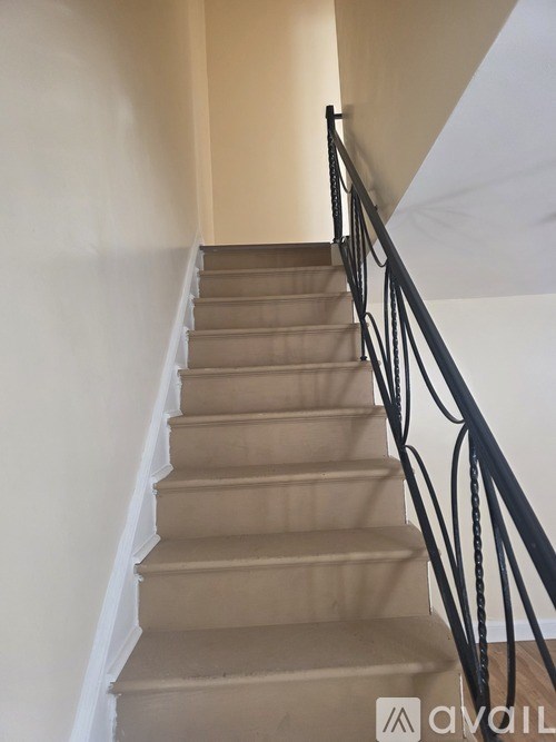 A staircase with beige carpeted steps and black metal railings.