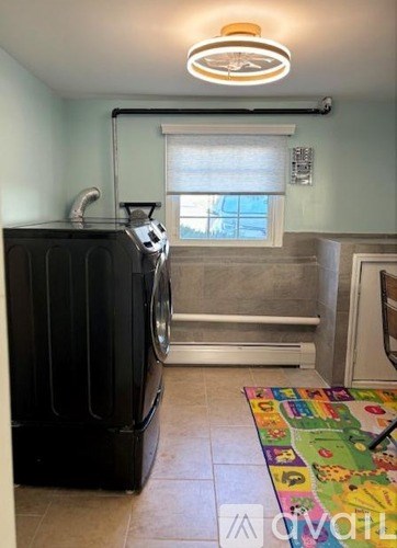 A black washing machine sits in a laundry room next to a window.