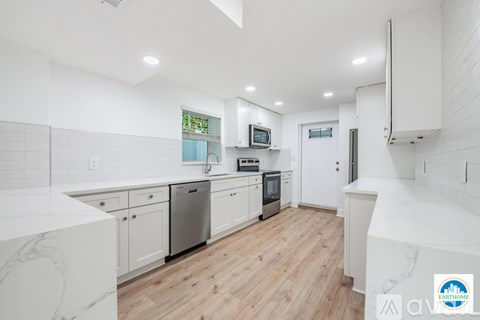 A modern kitchen with white cabinets and a wooden floor.