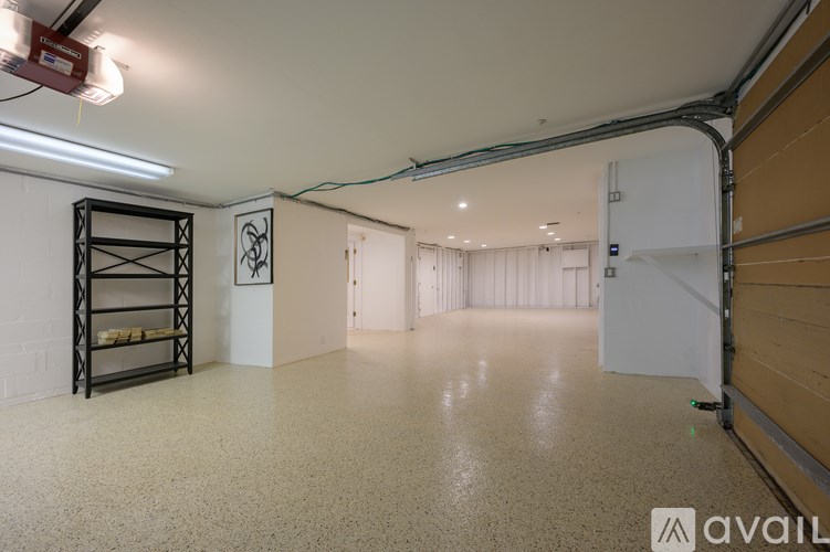 A spacious room with a white floor and walls, a black shelving unit, and a white door.