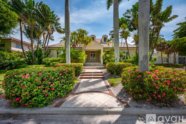 A beautifully landscaped entrance to a home with red flowers and palm trees.