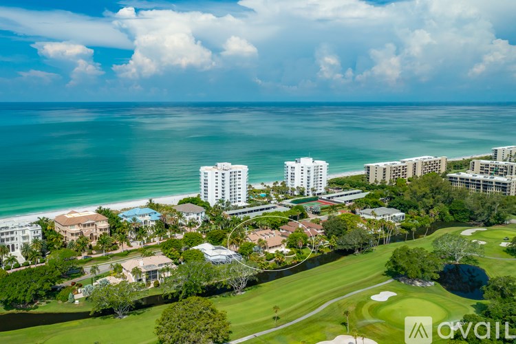 A golf course is surrounded by buildings and the ocean.