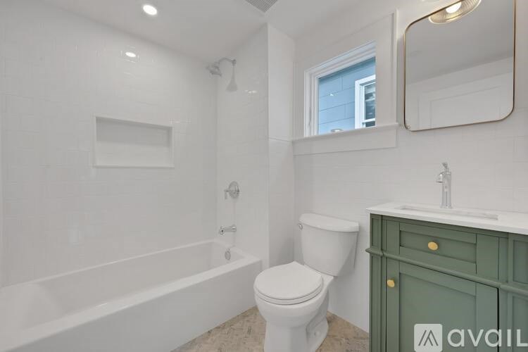 A white bathroom with a green cabinet and a window.