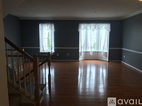 A spacious room with wooden floors and two windows.