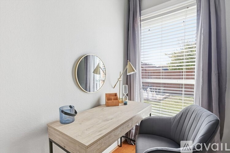 A desk with a mirror, lamp, and a blue container sits in front of a window with blinds.