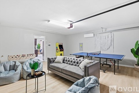A living room with a blue sofa, a grey armchair, a black coffee table, a blue table tennis table, and a green plant.