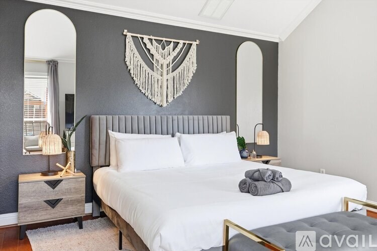 A bedroom with a large bed, a grey headboard, and a decorative wall hanging.
