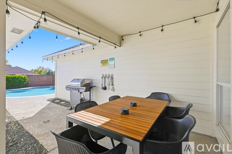 A wooden table with four chairs is set up under a covered patio area.