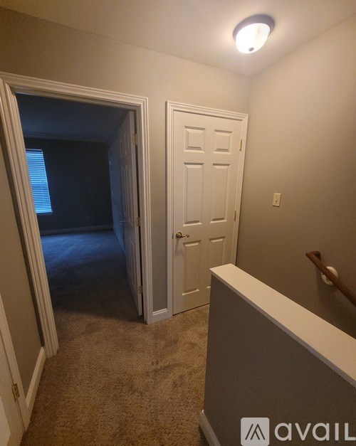 A room with a carpeted floor, a white door, and a white wall with a light switch.