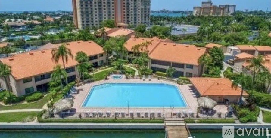 A large swimming pool is surrounded by a building and palm trees.
