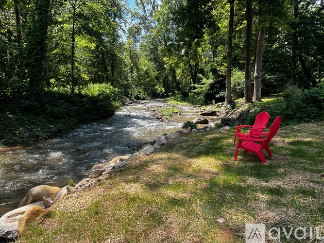 A red chair is placed on the grass near a river.