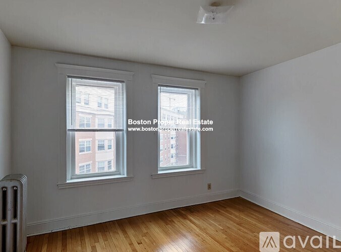 A room with wooden floors and two windows, one of which has a view of a building outside.