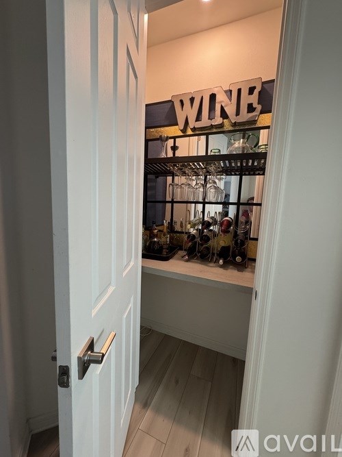 A white door with a handle and a sign that says "WINE" above a shelf with wine glasses and bottles.