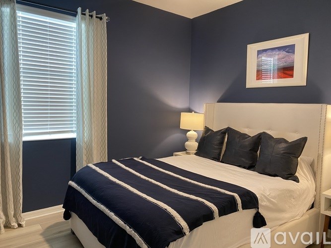 A bedroom with a large bed and a window with white curtains.