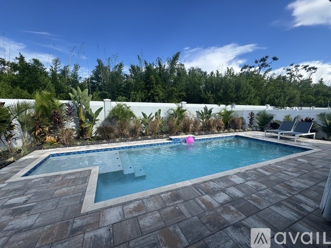A pool surrounded by a stone patio and a white wall with trees in the background.