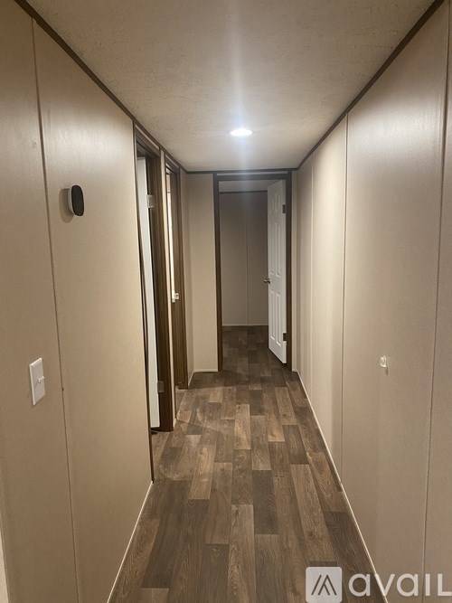 A long hallway with wood flooring and a light switch on the wall.