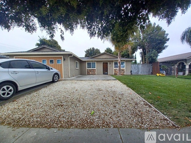 A silver car is parked in front of a house with a gravel driveway.