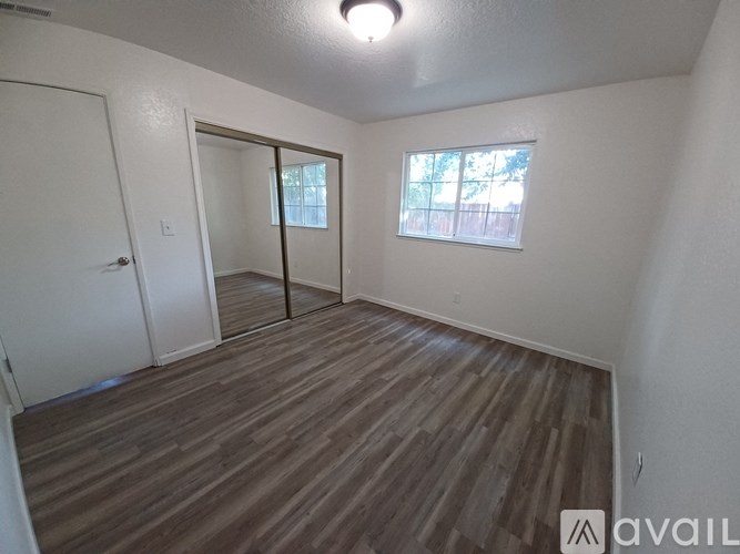 A room with wooden flooring and a window with a view of a fence.