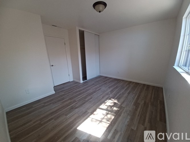 A room with wooden flooring and a window letting in sunlight.
