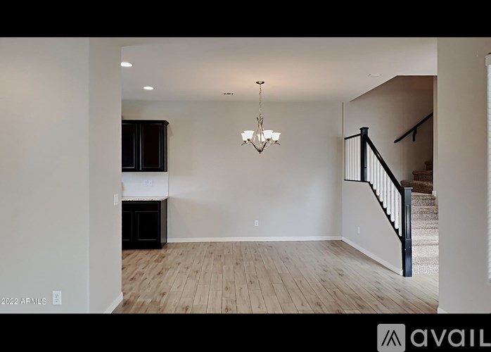 A chandelier hangs in a spacious room with wooden floors and white walls.
