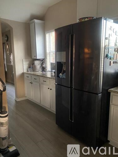 A black refrigerator is in a kitchen with white cabinets.