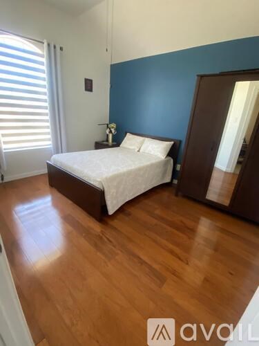 A bedroom with a bed, wooden floor, and a blue wall.