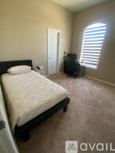 A bedroom with a bed, a chair, and a window with blinds.