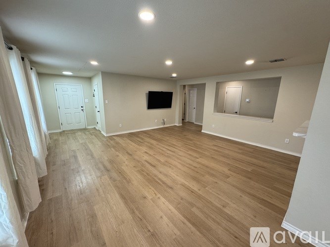 A spacious room with wooden flooring and a flat-screen TV mounted on the wall.