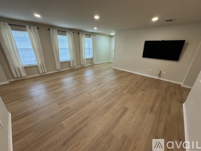 A spacious room with wooden flooring and a flat-screen TV mounted on the wall.
