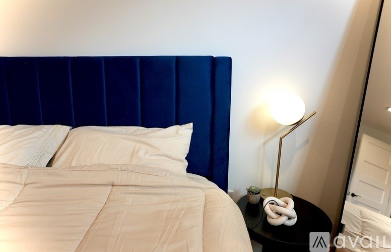 A bed with a blue headboard and white pillows is in a room with a lamp on a side table.