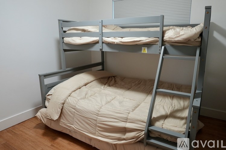 A bunk bed with a beige comforter is in a room with wooden floors and white walls.