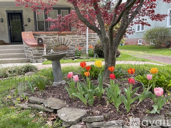A garden with a stone bench and a tree with red leaves.