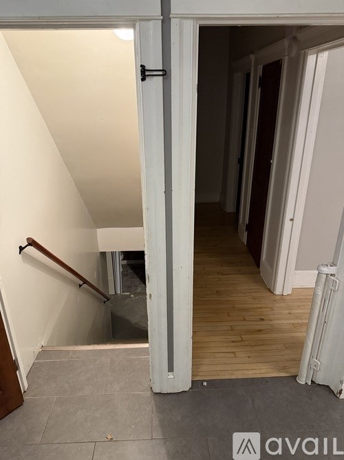 A hallway with a wooden floor and white walls leading to a door.