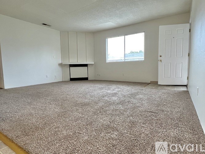 A room with a carpeted floor, a window, and a door.