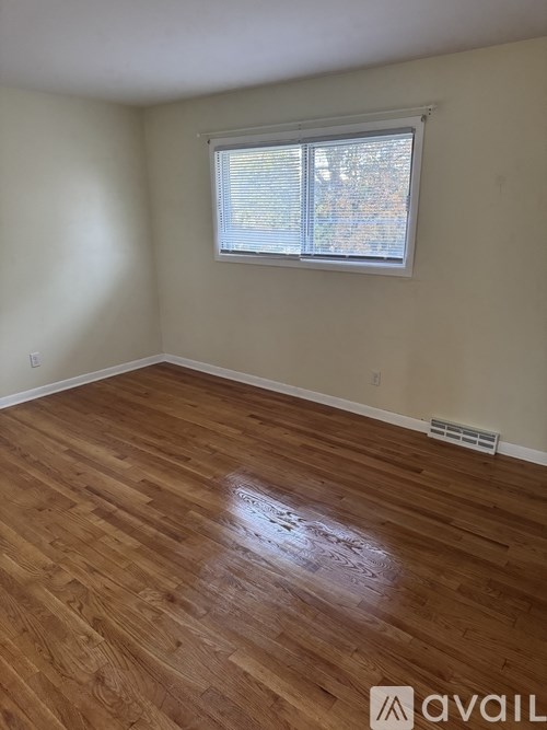 A room with wooden flooring and a window with blinds.