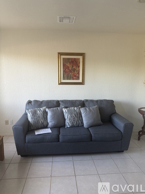 A grey couch with pillows and a painting on the wall.