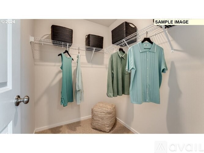 A white door is on the left of a hallway with clothes hanging on a rack and a basket on the floor.