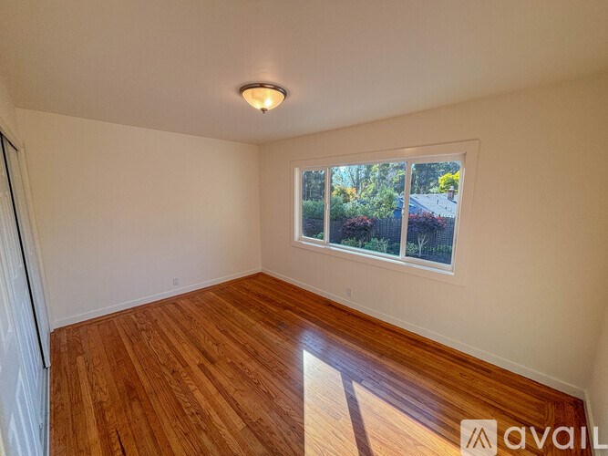 A room with wooden flooring and a window showing a view of a garden outside.