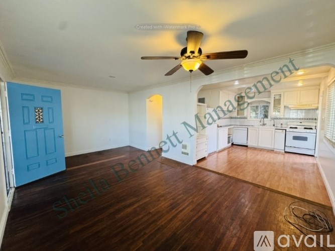 A room with a ceiling fan and a kitchen in the background.