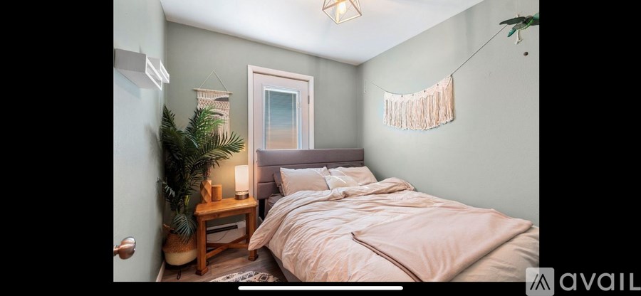 A bedroom with a bed, nightstand, and a plant.
