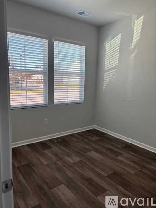 A room with wooden flooring and two windows with blinds.
