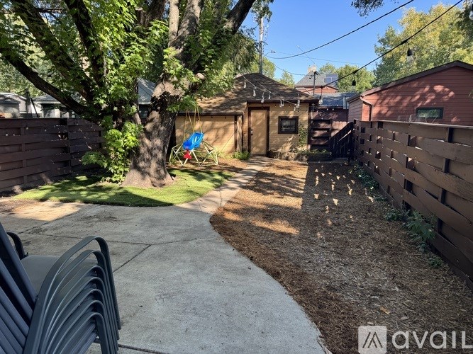 A backyard with a tree, a swing, and a wooden fence.