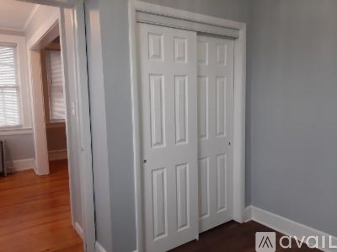A white door in a room with wooden floors and a window with blinds.
