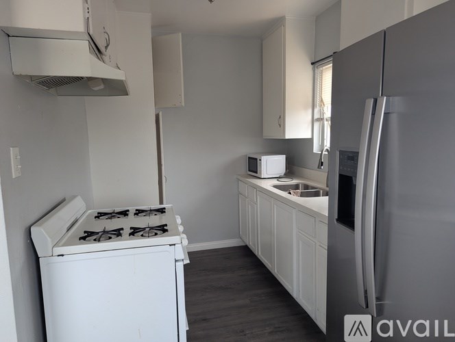 A kitchen with a white stove, white cabinets, and a silver refrigerator.
