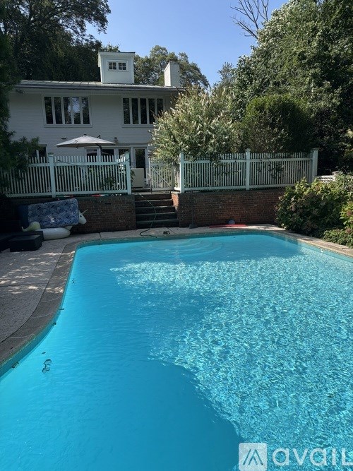 A pool in front of a house with a white fence.