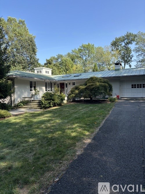 A white house with a green roof and a driveway in front.