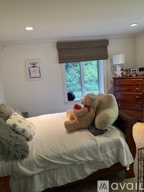 A bedroom with a bed, a teddy bear, and a dresser.